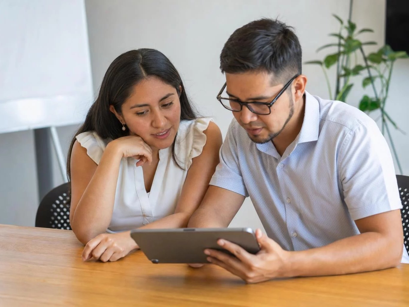 Dos colegas releyendo apuntes en una tablet apoyada en una mesa de madera