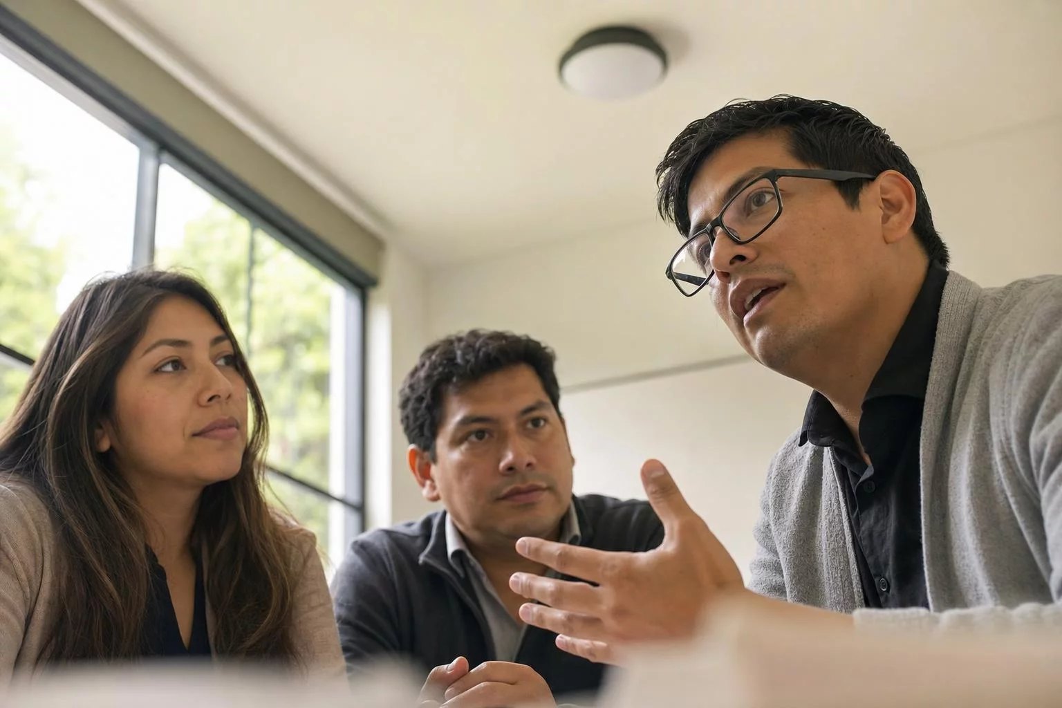 Tres profesionales en una sala de reuniones clara, uno de ellos explicando